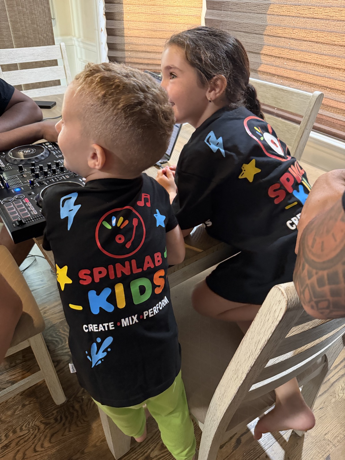 Young SpinLab Kids students wearing branded shirts while exploring a DJ controller